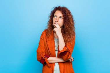 Genç kızıl saçlı zarif kadın şüpheli ve şüpheci ifade ile yana bakıyor.