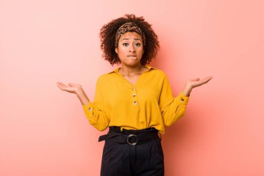 Pembe bir arka plan karşı Genç Afrikalı Amerikalı kadın karışık ve şüpheli omuzsilke omuzlar bir kopyasını alanı tutmak için.