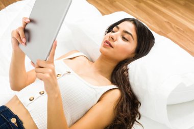 Tablet kullanarak yatakta yatan genç Arap kadın