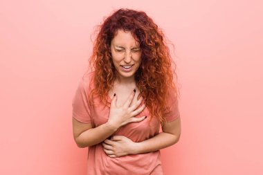 Genç doğal ve otantik kızıl saçlı kadın mutlu güler ve mide ellerini tutarak eğlenceli.
