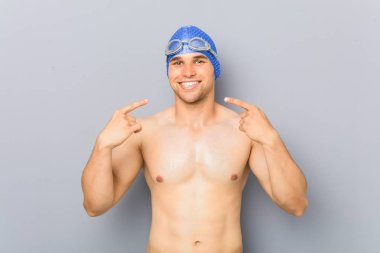 Genç profesyonel yüzücü adam gülümsüyor, ağızda parmaklarını işaret.