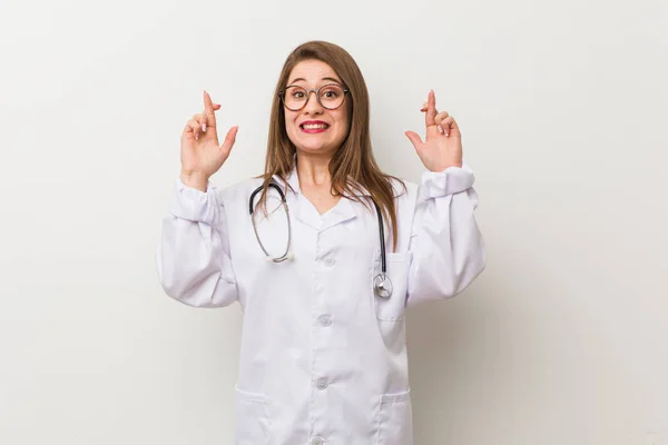 Νεαρή Γιατρός Γυναίκα Εναντίον Ενός Λευκού Τοίχου Διασχίζοντας Δάχτυλα Για — Φωτογραφία Αρχείου
