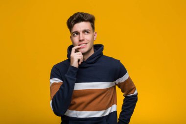 Young cool man wearing a hoodie relaxed thinking about something looking at a copy space.