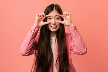 Young business chinese woman wearing pink suit keeping eyes opened to find a success opportunity.