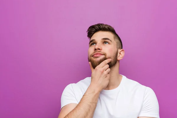 Young handsome caucasian man looking sideways with doubtful and skeptical expression.