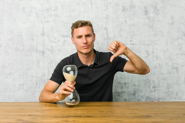 Jovem Segurando Temporizador Areia Uma Mesa Mostrando Polegar Para Baixo — Fotografia de Stock