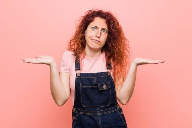 Genç güzel zencefil kızıl saçlı kadın bir kot dungaree şüphe giyen ve sorgulama jest omuzsa.