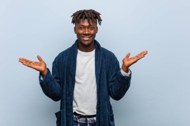 Genç Afrikalı siyah adam pijama giyen kolları ile ölçek yapar, mutlu ve kendinden emin hissediyor.