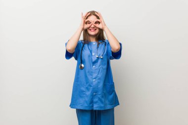 Gözleri üzerinde tamam işareti gösteren beyaz bir duvara karşı genç hemşire kadın