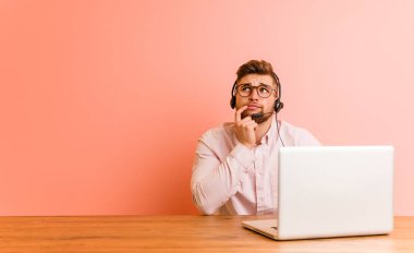 Bir çağrı merkezinde çalışan genç adam şüpheli ve şüpheci ifade ile yana bakıyor.