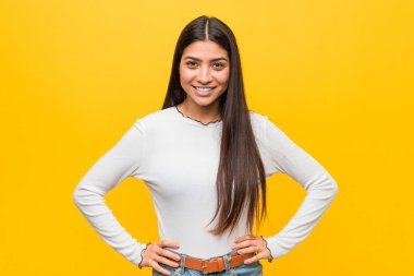 Sarı bir arka plan karşı genç güzel arap kadın emin kalça ellerini tutmak.