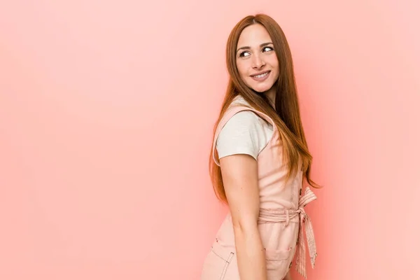 Young ginger woman with freckles looks aside smiling, cheerful and pleasant.