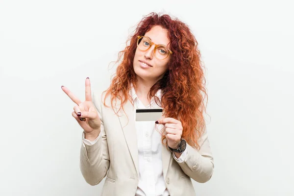 指でナンバー2を示すクレジットカードを持つ若い白人の赤毛の女性 — ストック写真