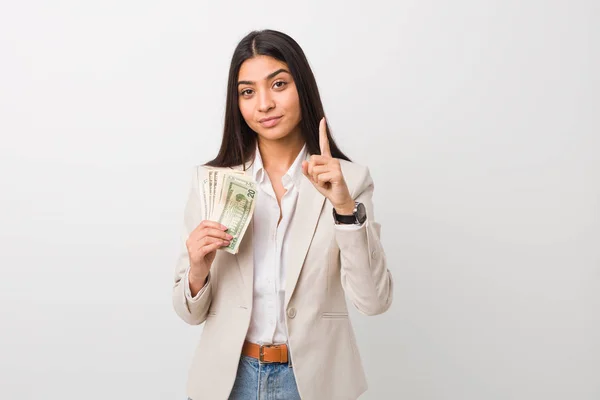 Young arab business woman holding dollars showing number one with finger.