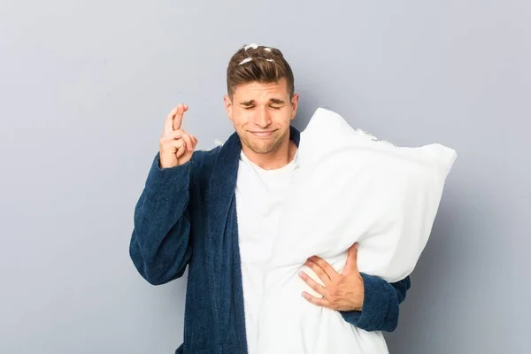 Young Man Wearing Pijama Holding Pillow Crossing Fingers Having Luck — Stock Fotó