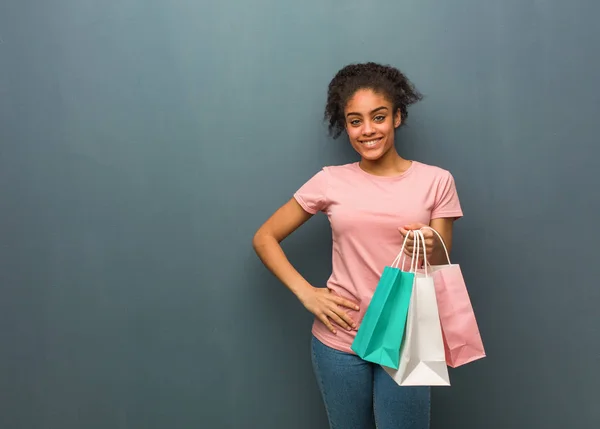 Young black woman with hands on hips. She is holding a shopping bags.