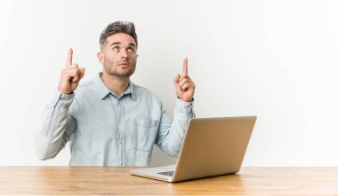 Genç ve yakışıklı bir adam laptopuyla çalışıyor ve ağzı açık bir şekilde yukarı bakıyor..