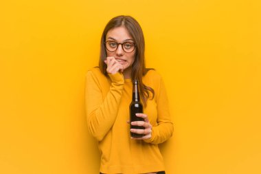 Tırnaklarını yiyip, gergin ve çok endişeli genç beyaz bir kadın. Elinde bira var..