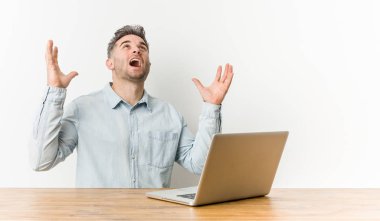 Young handsome man working with his laptop screaming to the sky, looking up, frustrated.