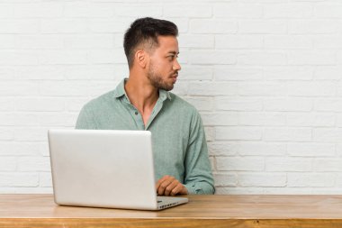 Genç filipinli adam dizüstü bilgisayar sola bakarak çalışan oturan, yanlara poz.