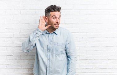 Bir dedikodu dinlemeye çalışan bir tuğla duvara karşı genç yakışıklı adam.