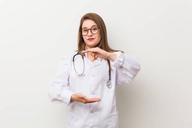 Genç doktor kadın beyaz bir duvara karşı iki eliyle bir şey tutan, ürün sunumu.