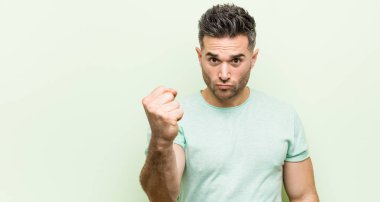Yeşil bir arka plan karşı genç yakışıklı adam kameraya yumruk gösteren, agresif yüz ifadesi.