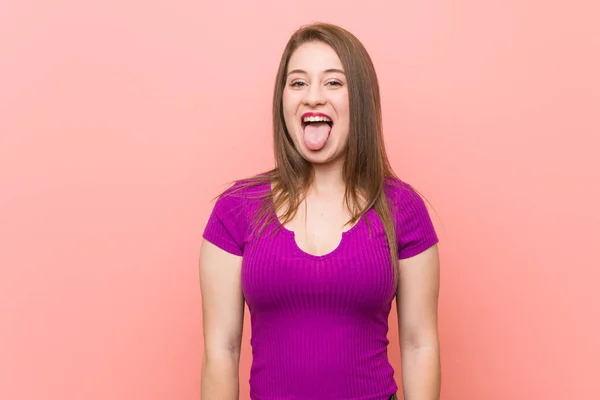 ピンクの壁に対する若いヒスパニックの女性面白いとフレンドリーな舌を突き出す — ストック写真