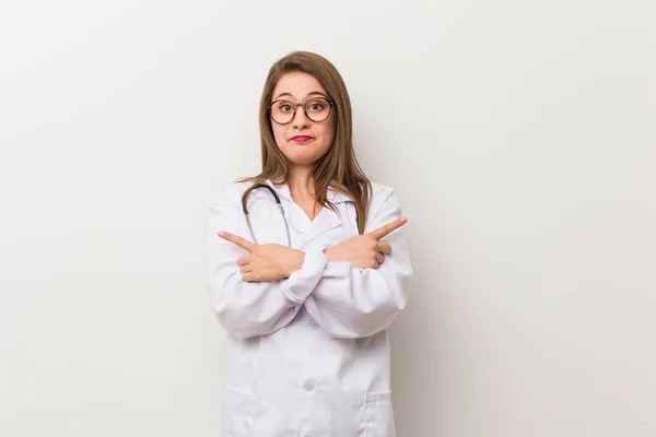 Jonge Dokter Vrouw Tegen Een Witte Muur Punten Opzij Probeert — Stockfoto
