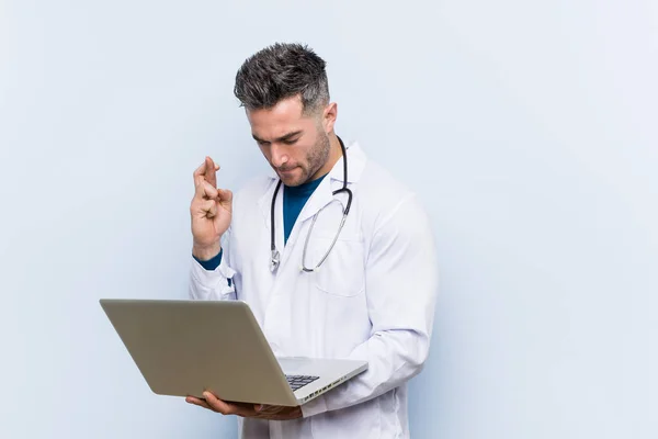 Caucasian Doctor Man Holding Laptop Crossing Fingers Having Luck — Stok fotoğraf