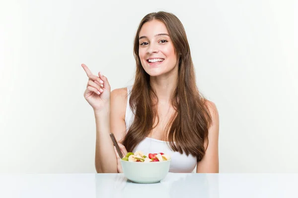 Giovane Donna Caucasica Mangiare Frutta Ciotola Sorridente Allegramente Indicando Con — Foto Stock