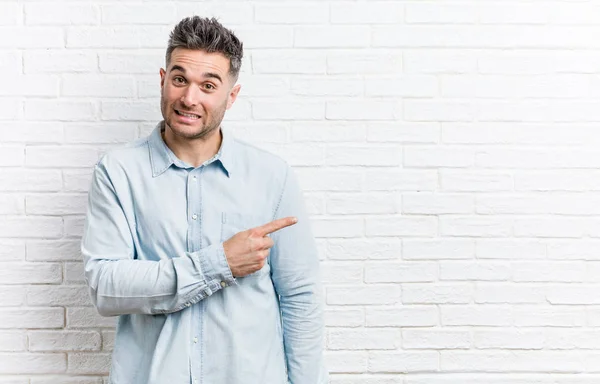 Jovem Homem Bonito Contra Uma Parede Tijolos Sorrindo Apontando Para — Fotografia de Stock