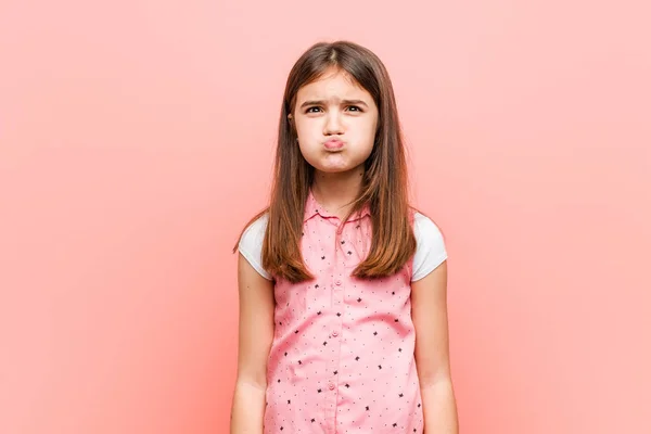 Cute little girl blows cheeks, has tired expression. Facial expression concept.
