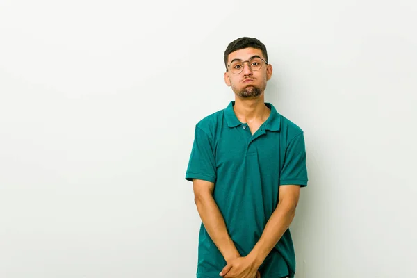 Young hispanic man blows cheeks, has tired expression. Facial expression concept.