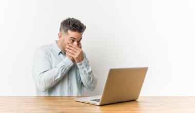 Dizüstü bilgisayarıyla çalışan genç yakışıklı adam elleriyle ağzını kapatarak şok eve.