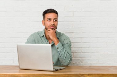 Genç Filipino adam oturan onun laptop ile yan şüpheli ve şüpheci ifade bakıyor.
