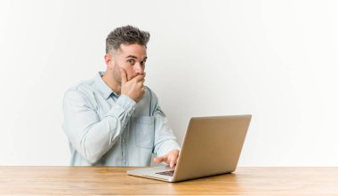 Genç yakışıklı adam el ile ağız kapsayan bir kopya alanı arayan düşünceli dizüstü bilgisayar ile çalışan.