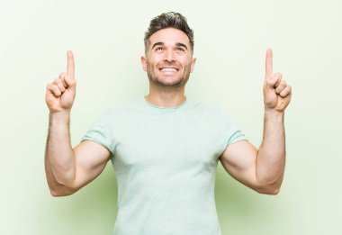 Yeşil bir arka plan karşı Genç yakışıklı adam boş bir boşluk gösteren kadar her iki ön parmak ile gösterir.