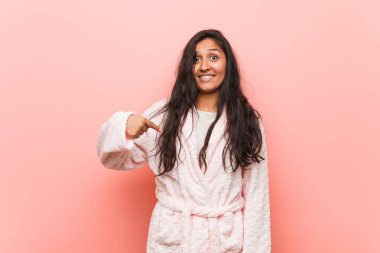 Young indian woman wearing pajama person pointing by hand to a shirt copy space, proud and confident