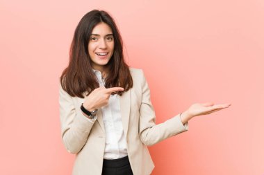 Pembe bir arka plan karşı Genç esmer iş kadını avuç içi bir kopya alanı tutarak heyecanlı.