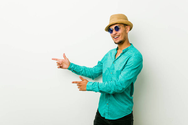 Young hispanic man wearing a summer clothes excited pointing with forefingers away.