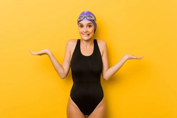 Young swimmer caucasian woman confused and doubtful shrugging shoulders to hold a copy space.