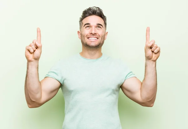 Junger Gutaussehender Mann Vor Grünem Hintergrund Deutet Mit Beiden Erhobenen — Stockfoto