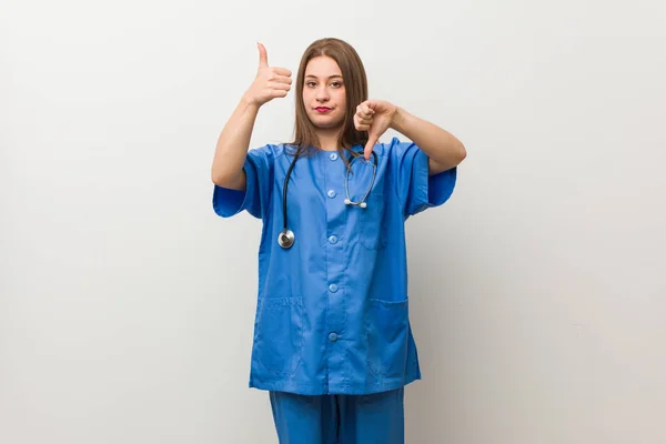 親指を上にして親指を下に示す白い壁に対する若い看護師の女性は 難しい選択の概念 — ストック写真