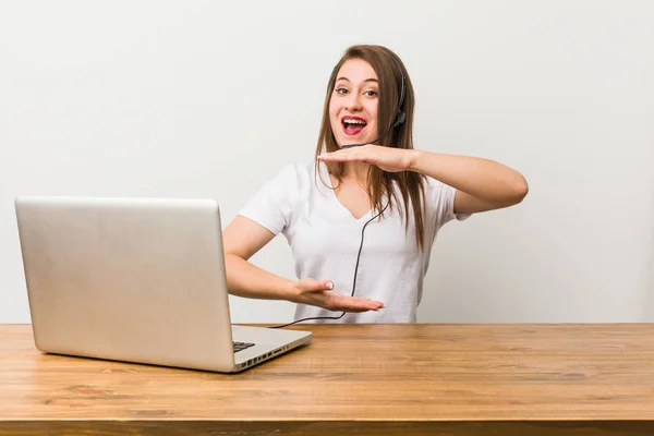 Young telemarketer woman holding something with both hands, product presentation.