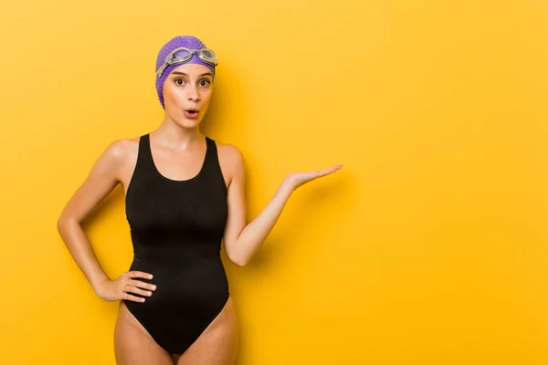 Young swimmer caucasian woman impressed holding copy space on palm.