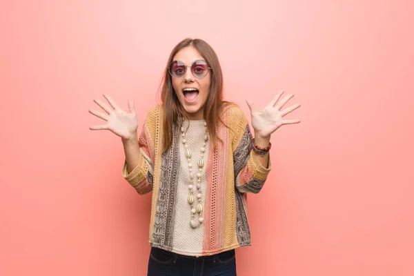 Young hippie woman on pink background celebrating a victory or success