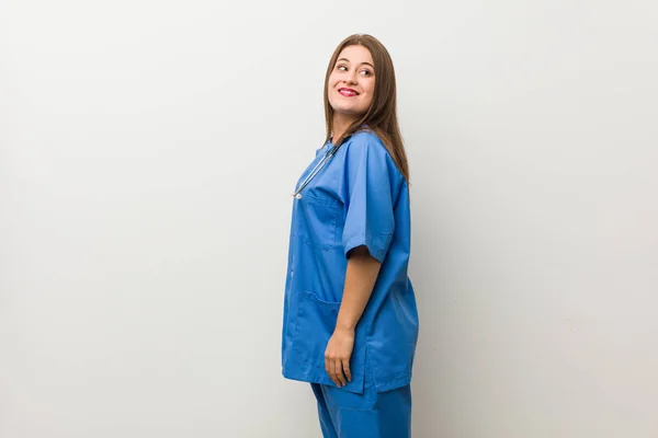 Νεαρή Νοσοκόμα Γυναίκα Εναντίον Ενός Λευκού Τοίχου Κοιτάζει Στην Άκρη — Φωτογραφία Αρχείου