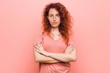 Kendinden emin hisseden genç, doğal ve otantik kızıl saçlı kadın, kararlılıkla kolları keserek.