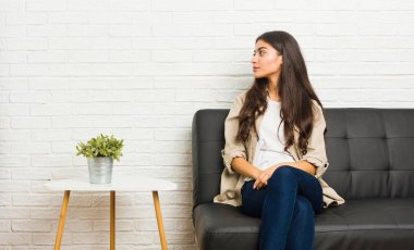 Kanepede oturan genç Arap kadın sola bakıyor, yanlara doğru poz veriyor.